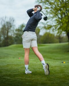 Golfer performing a controlled trunk rotation stretch beside a golf bag before practice.